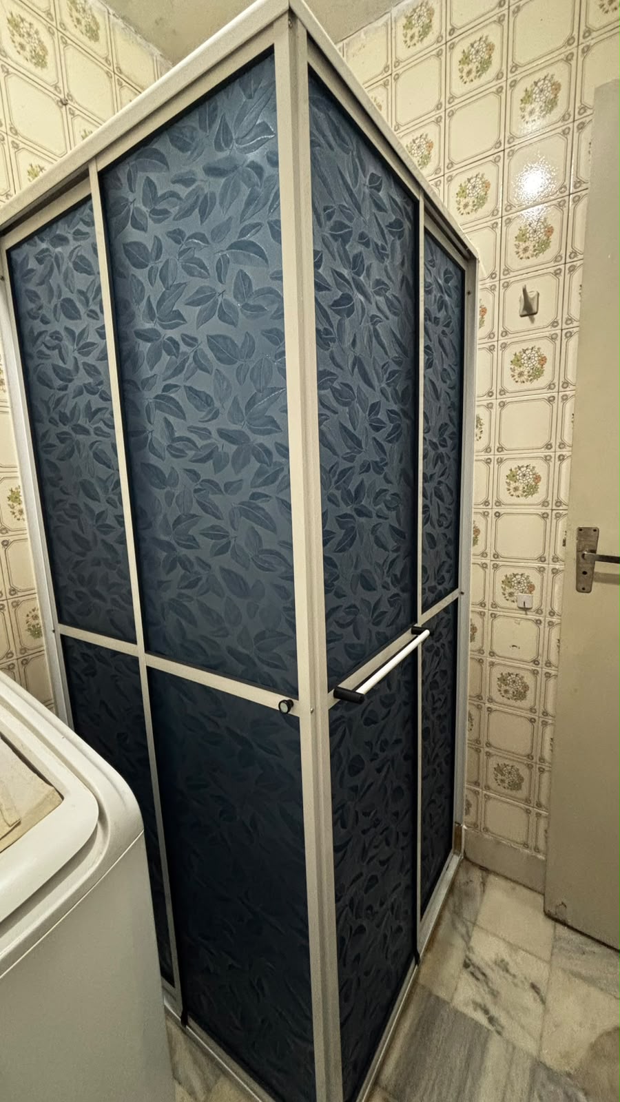 armário de cozinha ou banheiro com portas de vidro azul estampado com folhas e moldura branca, em ambiente com