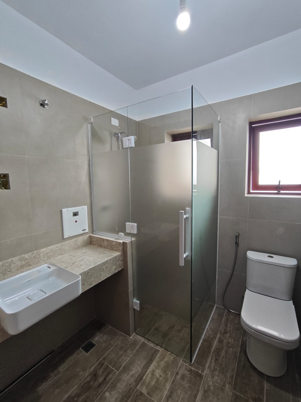 um banheiro moderno com banheira de vidro, pia de granito, toilette e janela — texto: