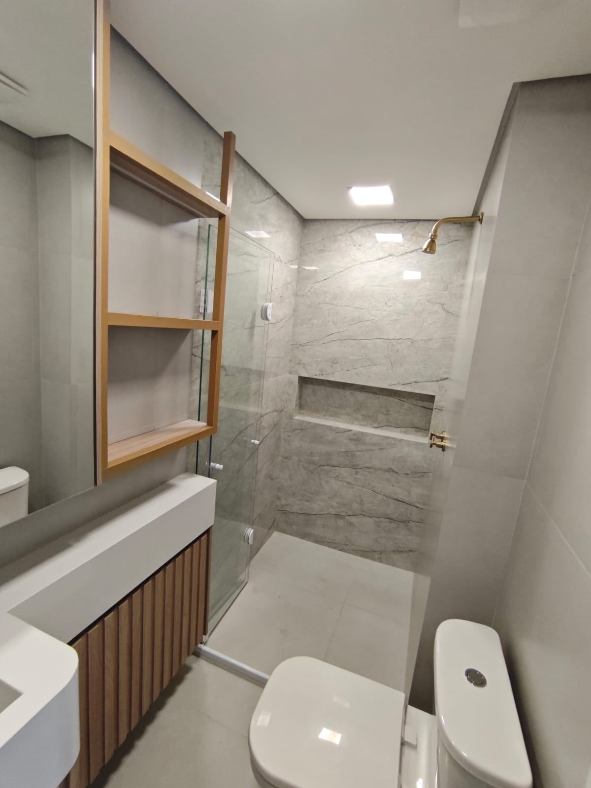 uma foto de um banheiro moderno com banheira de chuveiro, toilette, pia e prateleira de madeira — texto: