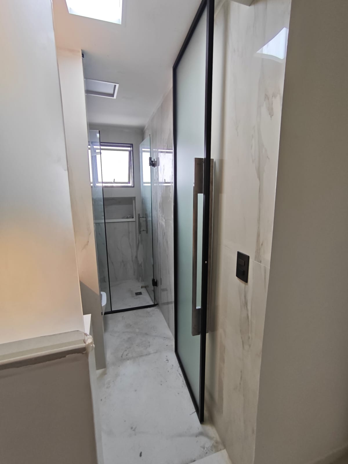 uma foto de um banheiro moderno com piso e paredes de mármore branco, janela e porta de vidro para chuveiro